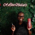 Business and marketing major Alyssa Parker, 24, holds a nail enamel spray and drill tool in front of a greenery backdrop, displaying her Hawthorne at-home nail studio name “A List Nailz” on Friday, April 17.