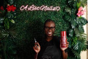 Business and marketing major Alyssa Parker, 24, holds a nail enamel spray and drill tool in front of a greenery backdrop, displaying her Hawthorne at-home nail studio name “A List Nailz” on Friday, April 17.